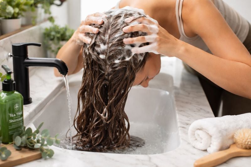 Scalp massage for hair growth while shampooing at bathroom sink.